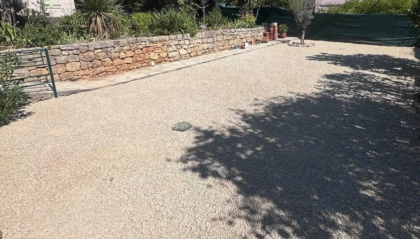 Cour recouverte de gravier clair le long du muret en pierre, après travaux